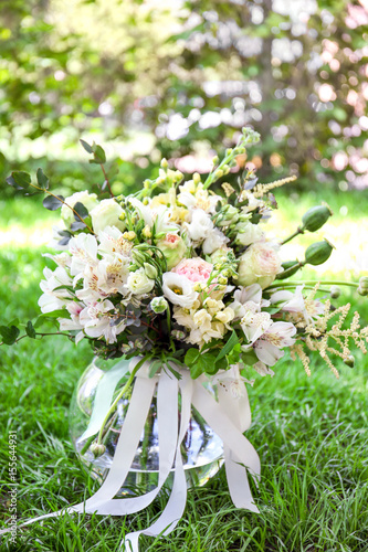 Festive vase with beautiful bouquet of different flowers on grass in garden