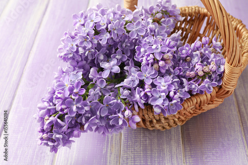 Wicker basket with beautiful bouquet of lilac flowers on wooden table