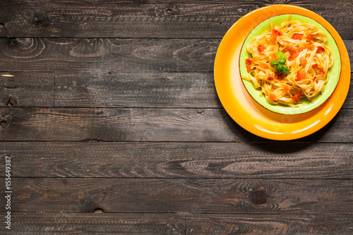 Tagliatelle with tomato and basil, made at home, on a wooden background.