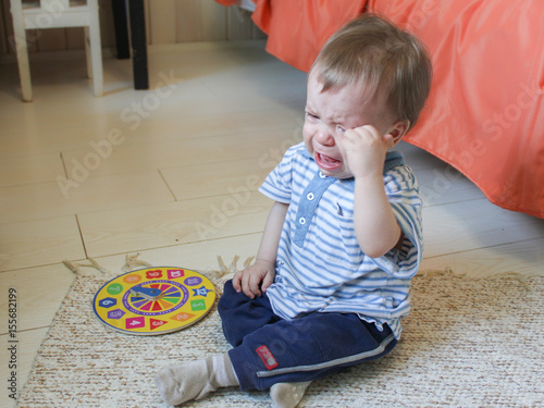 Little boy sitting on the floor, he's upset and crying. The child is crying sitting on the floor in the room..