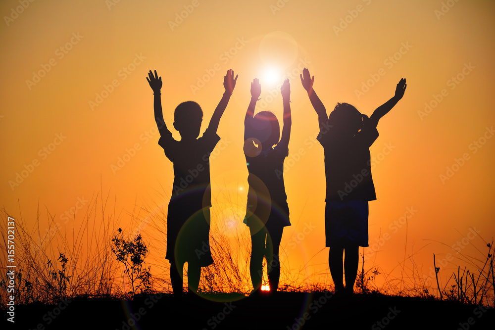The silhouette of three children who are friends on sunset background.Effect Flare image. The silhouette of three children who are friends on sunset background.Effect Flare image.