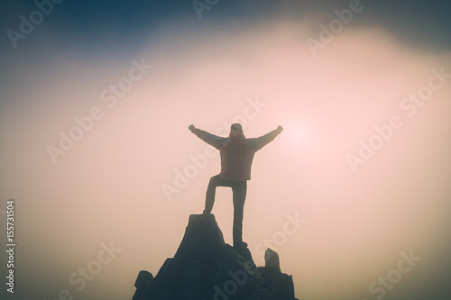 Hiker with raised hands standing on a cliff. Instagram stylization