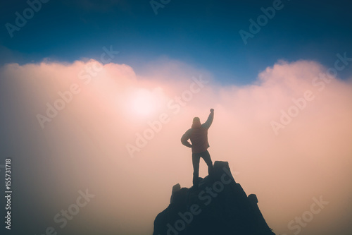 Hiker with raised hand standing on a cliffs edge. Instagram stylization