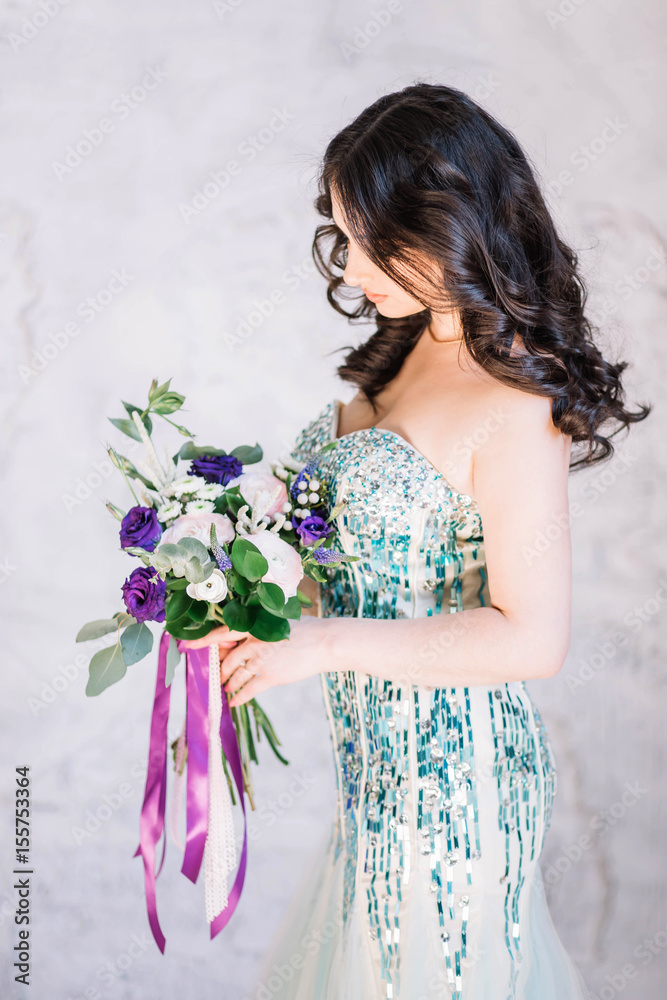 beautiful sexy Oriental girl with makeup black curls in a bright green sequined dress with purple and pink bouquet on his hand looking down profile on white gray background beautiful sexy Oriental girl with makeup black curls in a bright green sequined dress with purple and pink bouquet on his hand looking down profile on white gray background