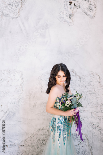 Beautiful girl bride brunette with professional makeup curls in a green lime dress with glitter sparkles with a delicate bouquet in his hand looking down with a smile on white background Studio © liliyabatyrova