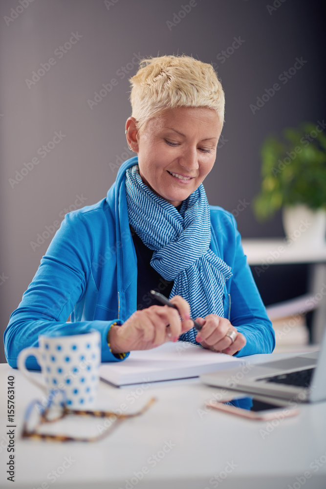 Businesswoman using laptop and drinking coffee while sitting in modern office Businesswoman using laptop and drinking coffee while sitting in modern office