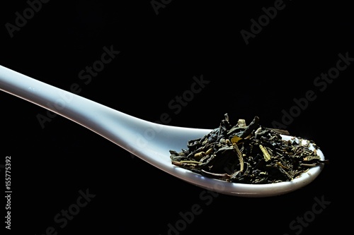 Mixture of green tea Camellia sinensis and morrocan mint Metha Spicata Nana on white laboratory ceramic spoon, black background photo