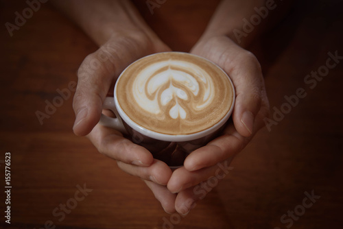 Male hands holding a cup of coffee on wooden table