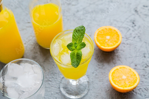 Fresh Orange Juice in Glass and Bottles and some Ripe Oranges on Grey Background. Healthy Drink, diet or Detox.
