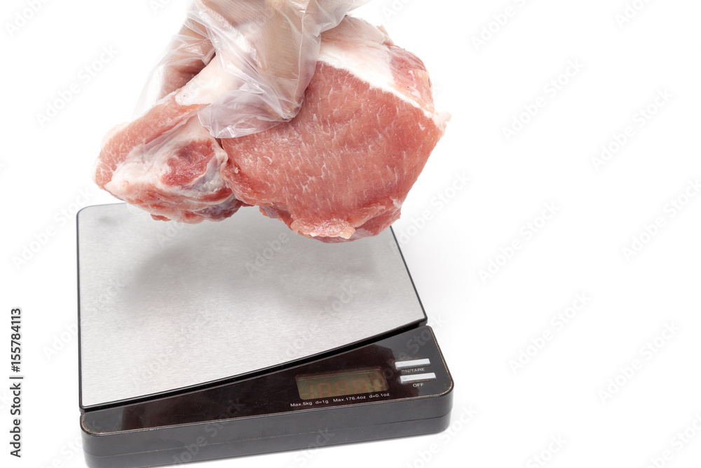 Raw pork meat is prepared to weight on the digital scale on white background isolated