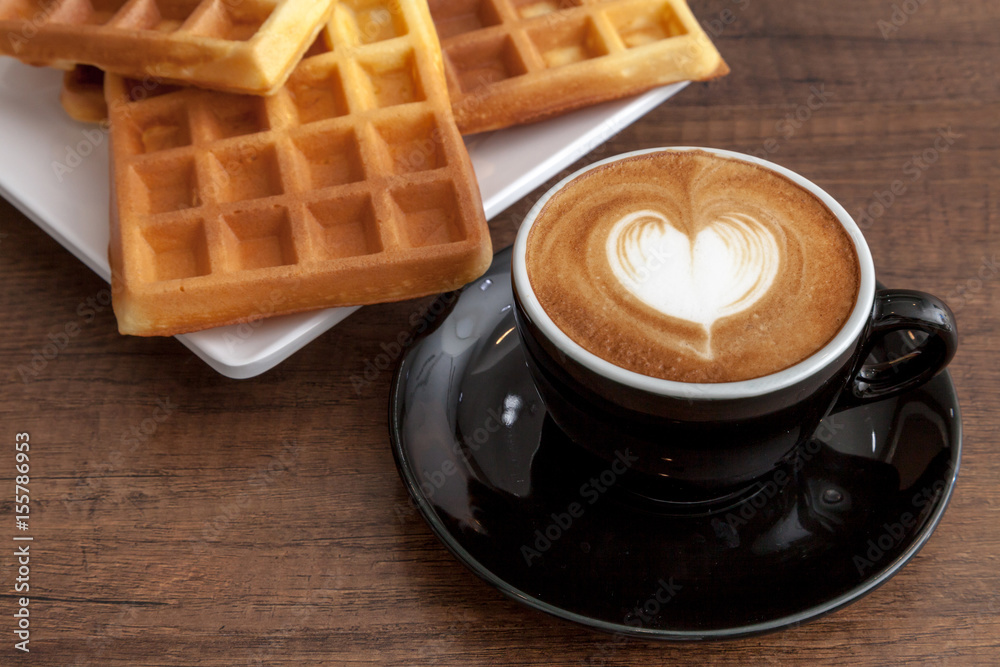 Coffee cup of latte art heart shape beside with some waffle on wooden background