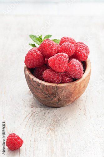 Fresh raspberries in  olive wooden bowl  on  old  wooden board, with copy space. Selective focus.