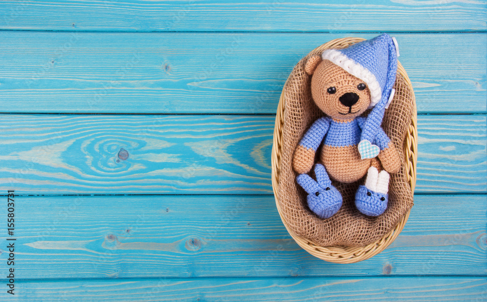 Obraz premium Small knitted bear lying in a basket on a blue wooden background. Teddy bears crocheted. Copy space