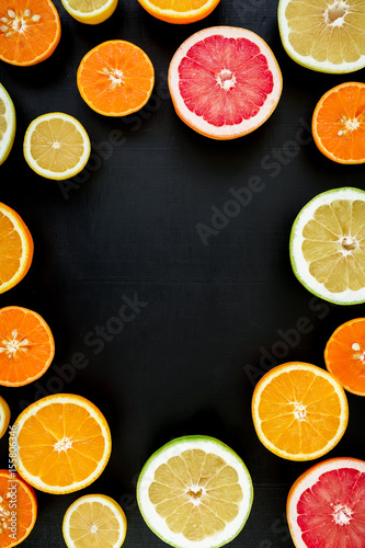 Round frame made of oranges, grapefruit and lemon isolated on black background. Flat lay, top view. Tropical summer mix of fruits