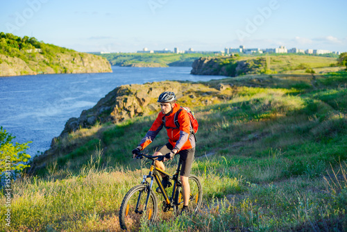 Cyclist in Red Jacket Riding Mountain Bike on the Beautiful Spring Trail above Blue River. Travel and Adventure Sport Concept