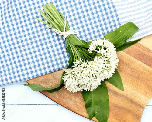 a bunch of wild garlic foraged for cooking on a blue gingham table cloth and wooden chopping board 
