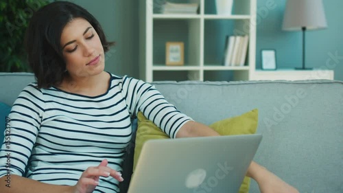 Young brunette woman working with laptom and making call on her cell phone at home photo