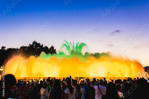 Silhouette of people watching at colorful illuminated musical fountains in the evening. Light and water night show perfomance. Montjuic Magic Fountain, Barcelona, Catalonia, Spain.