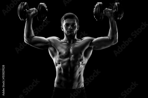 Black and white studio shot of a handsome young shirtless weightlifter exercising with dumbbells lifting weights athlete athletics activity lifestyle motivation power sports confidence focusing.