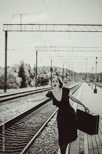 Gorgeous redhead woman in green velvet dress in vintage style with a suitcase on the platform