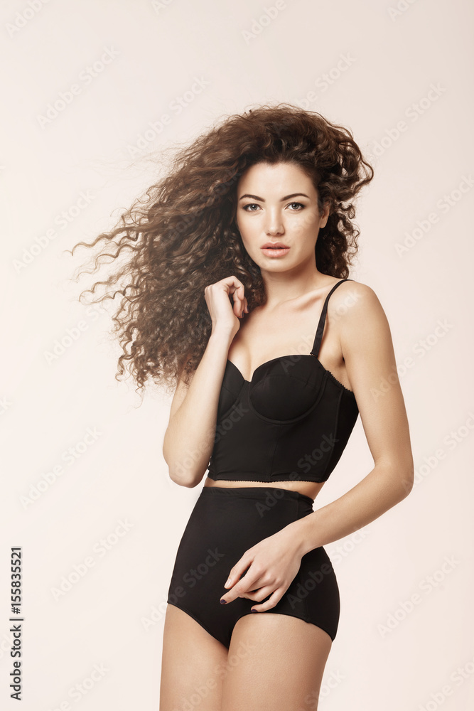 Fototapeta premium Beautiful model with flying curly hair in black underwear posing looking at camera.