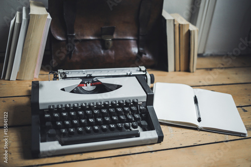 A vintage gray typewriter on a wooden floor. Notepad, pen, books and leather briefcase on the wooden floor
