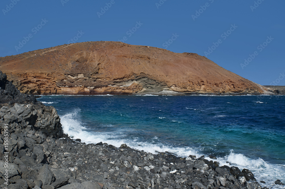 Horizontal shot of Montana Amarilla, the yellow mountain, and its popular seafront rocks degraded by erosion, with a small rough beach, popular natural tourist attraction in Tenerife.