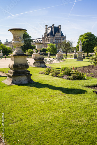 View of the Tuileries garden in Paris by a sunny morning with a carved vase in the foreground and the Flore pavilion of the Louvre palace in the background