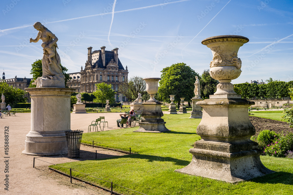 View of the Tuileries garden in Paris by a sunny morning with the statue of Medea and a carved vase in the foreground and the Flore pavilion of the Louvre palace in the background