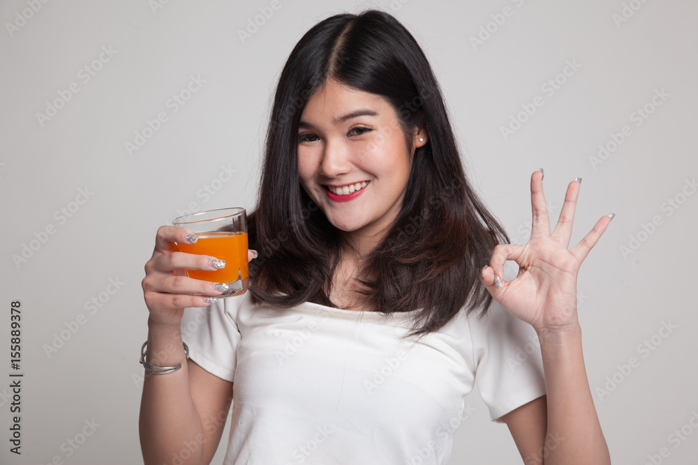 Young Asian woman drink orange juice show OK sign.