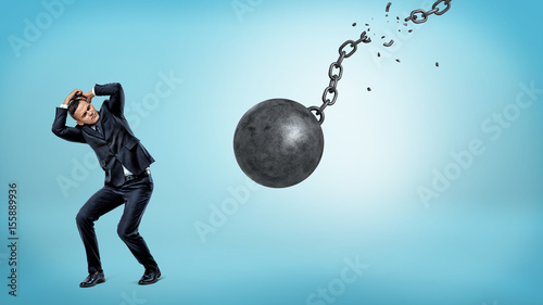 Schilderij op canvas A small businessman trying to hide and cover himself from a falling wrecking ball with a torn chain