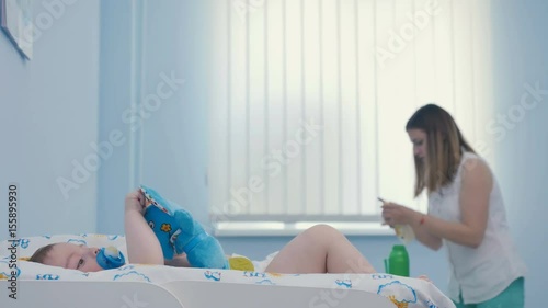 Mother prepare mixture in bottle on blurs background and little boy lay on nappy