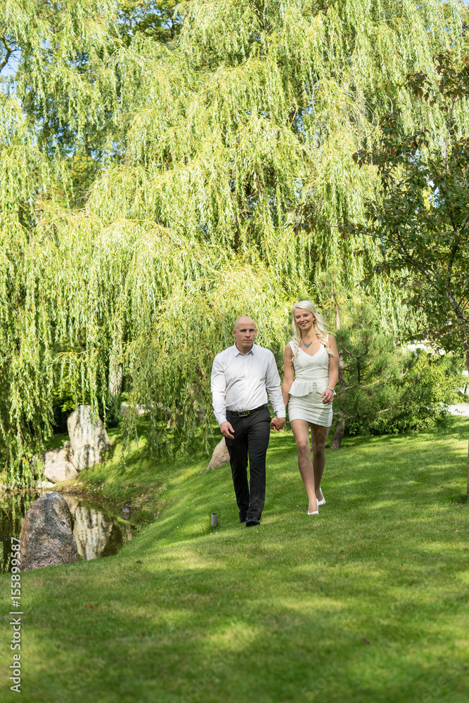 Happy couple holding hands and walking in grass. Man and woman in love. Young people resting in park, nature background Happy couple holding hands and walking in grass. Man and woman in love. Young people resting in park, nature background