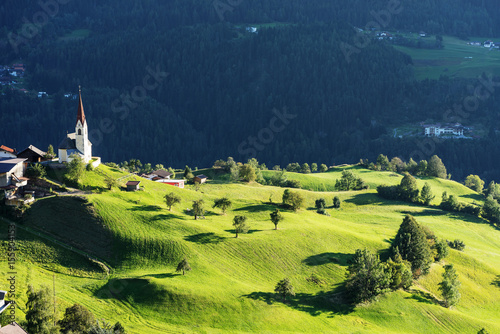 Chapel and sheep on the meadow. Bell tower, trees, shrubs and hilly green grassland. Heiliger Antoniuse church and houses in the evening light. Pitburger See, Taxegg, Salzburg, Austria, Europe photo