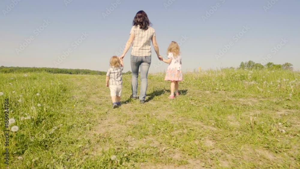 Family mother with her son and daughter are walking around the field. Walk in the fresh air. Summer sunny day. Slow Motion. Family mother with her son and daughter are walking around the field. Walk in the fresh air. Summer sunny day. Slow Motion.