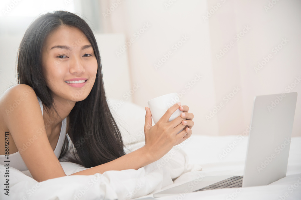 Happiness Asian girl smiling and holding cup of coffee with laptop on her bed. Happiness Asian girl smiling and holding cup of coffee with laptop on her bed.