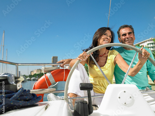 Mature couple at wheel of yacht smiling