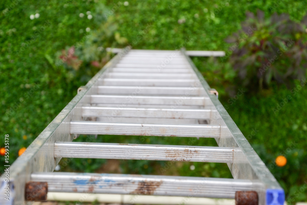Top view of a long silver aluminum ladder leaning against the wall of the house. Close up view from top of tall step ladder at roof. work at height. Ladder for workers, painters, engineers, repairman Top view of a long silver aluminum ladder leaning against the wall of the house. Close up view from top of tall step ladder at roof. work at height. Ladder for workers, painters, engineers, repairman