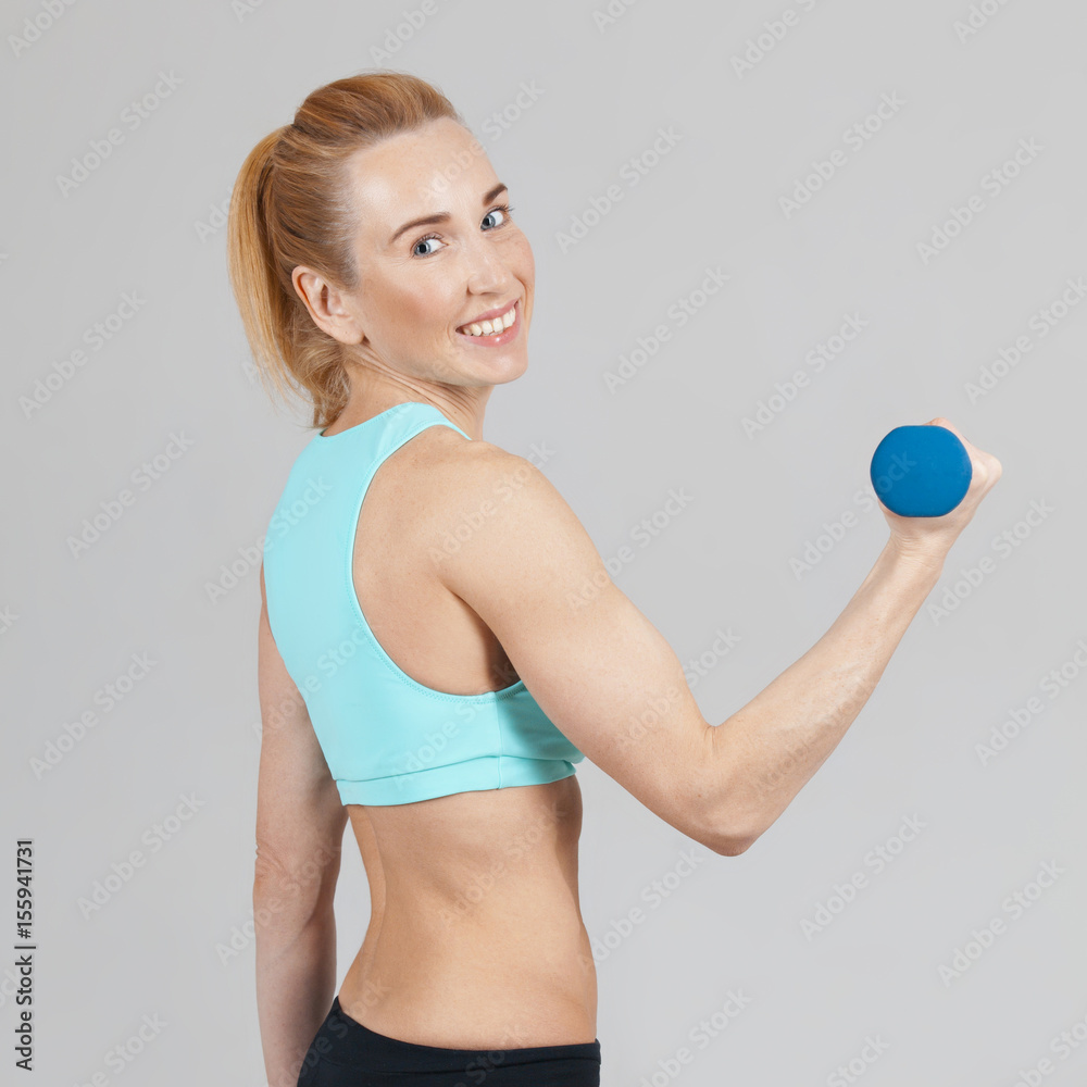happy middle-aged athletic woman working out with dumbbells on the grey background
