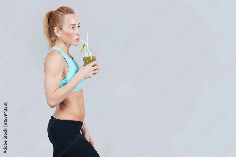 middle-aged athletic slim woman drinking the fresh fruit juice on the grey background middle-aged athletic slim woman drinking the fresh fruit juice on the grey background