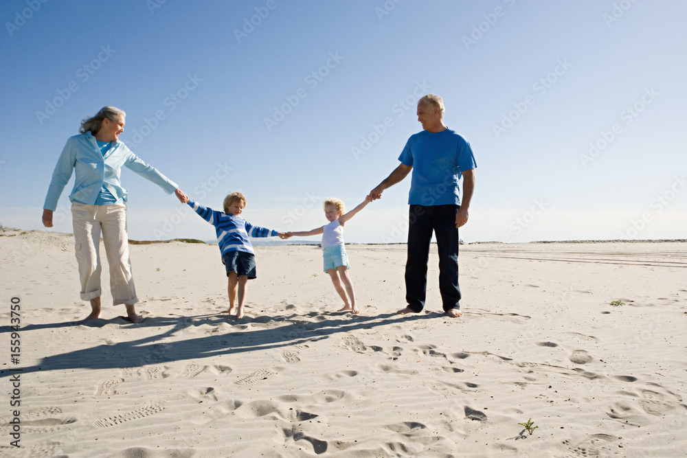 Grandparents and grandchildren holding hands, walking on beach