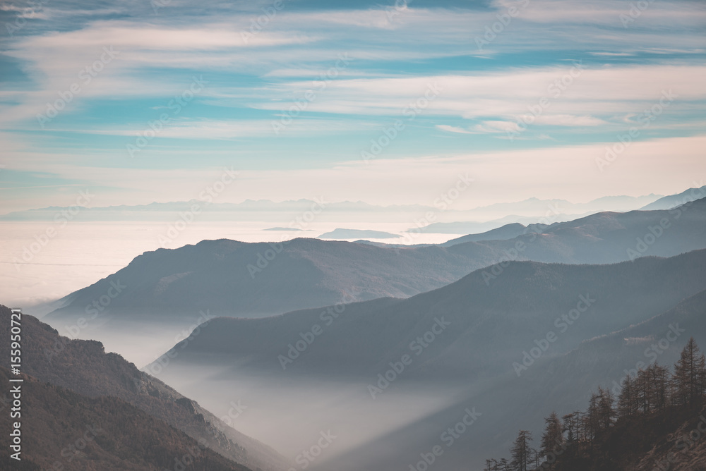 Distant mountain range with fog and mist covering the valleys below.Italian Alps, toned image.
