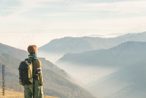 Female hiker with backpack looking at the majestic view on the italian Alps. Mist and fog in the valley below, snowcapped mountain peak in the background. Selective focus, toned image. © fabio lamanna