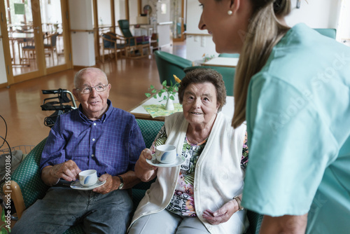 Nurse serving coffee to senior man and woman in retirement home