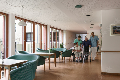 Nurses pushing senior man and woman in wheelchair trough the hall of nursing home