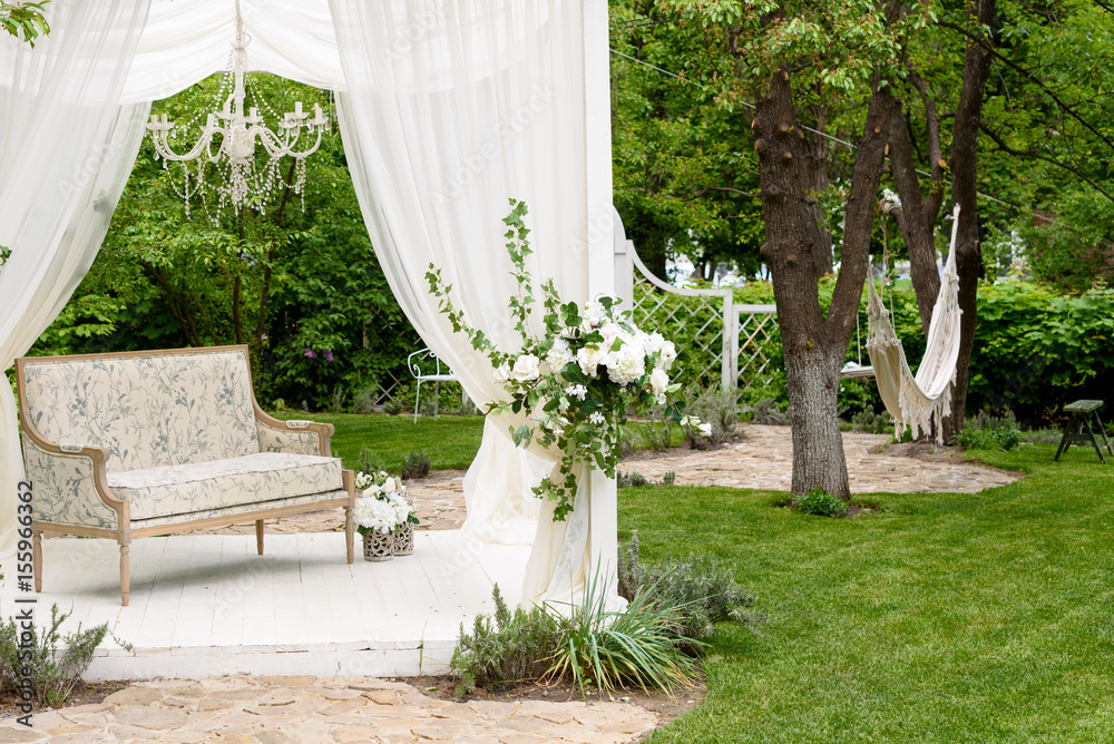 White vintage sofa with tent and flowers in a green garden