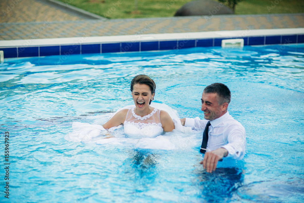 Young couple jumping in the swimming pool in a wedding suit and wedding dress. Sunny day. Young couple jumping in the swimming pool in a wedding suit and wedding dress. Sunny day.