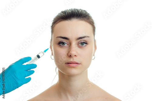 cosmetologist makes injection syringe on the face of a young beautiful girl who looks straight close-up