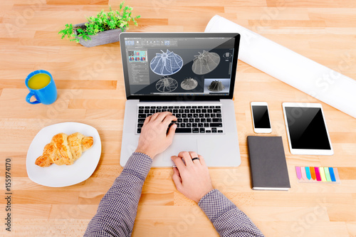 Engineer's workplace with laptop, mockup tablet, glasses, sketching, mockup smartphone, blue cup, croissant. Engineer  working on the laptop with 3d model of turbine for heavy industry
