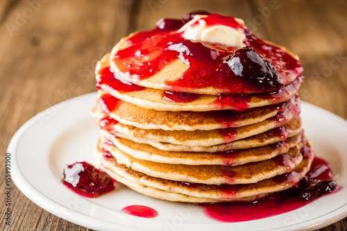 Pancakes with butter and jam on wooden table.